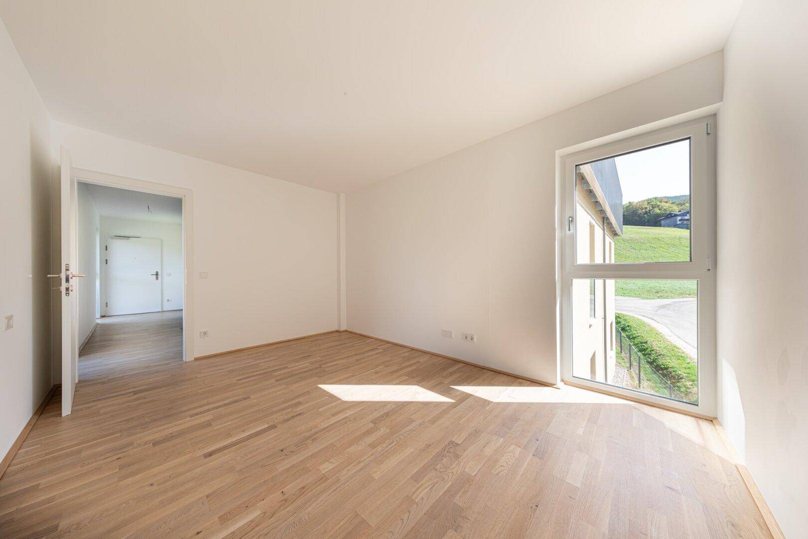 Geräumiges Schlafzimmer mit hellem Parkettboden und einem hohen Fenster für viel Tageslicht.