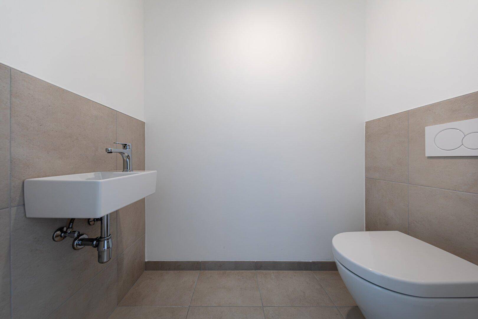 Modernes Gäste-WC mit Wand-WC, kleinem Waschbecken und beigefarbenen Fliesen.