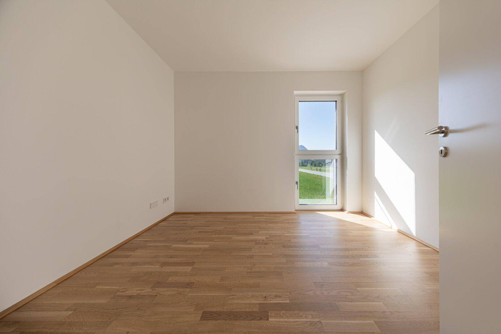 Geräumiges Schlafzimmer mit hellem Parkettboden und einem Fenster, das den Raum erhellt.