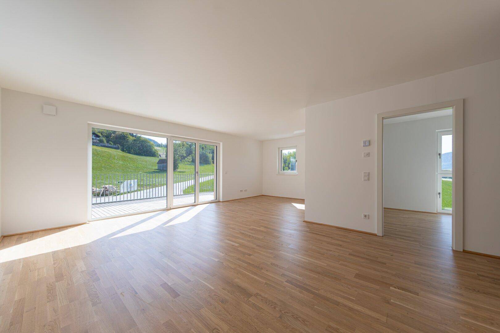 Helles Wohnzimmer mit Eichenparkett, großen Schiebetüren und Zugang zum Balkon mit Landschaftsblick.