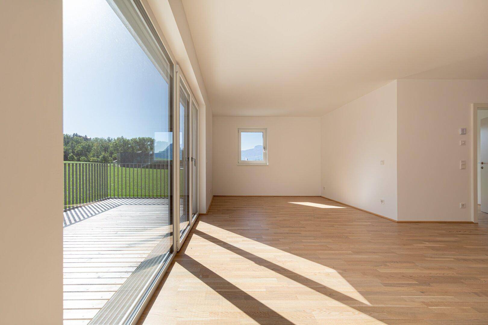 Lichtdurchflutetes Wohnzimmer mit großzügigen Fensterfronten und direktem Zugang zur sonnigen Terrasse.