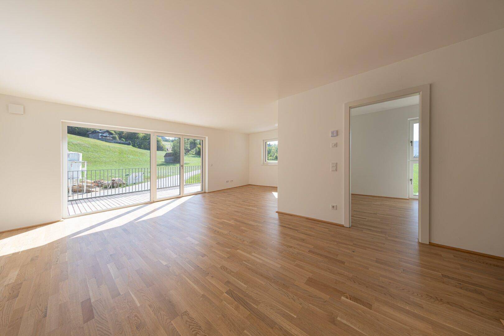 Helles Wohnzimmer mit Eichenparkett, großen Schiebetüren und Zugang zum Balkon mit Landschaftsblick.