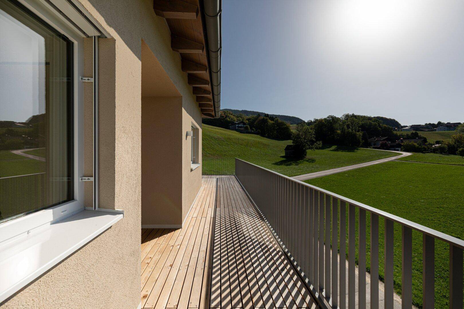 Heller Balkon mit Holzboden und weitem Blick über die grüne Landschaft.