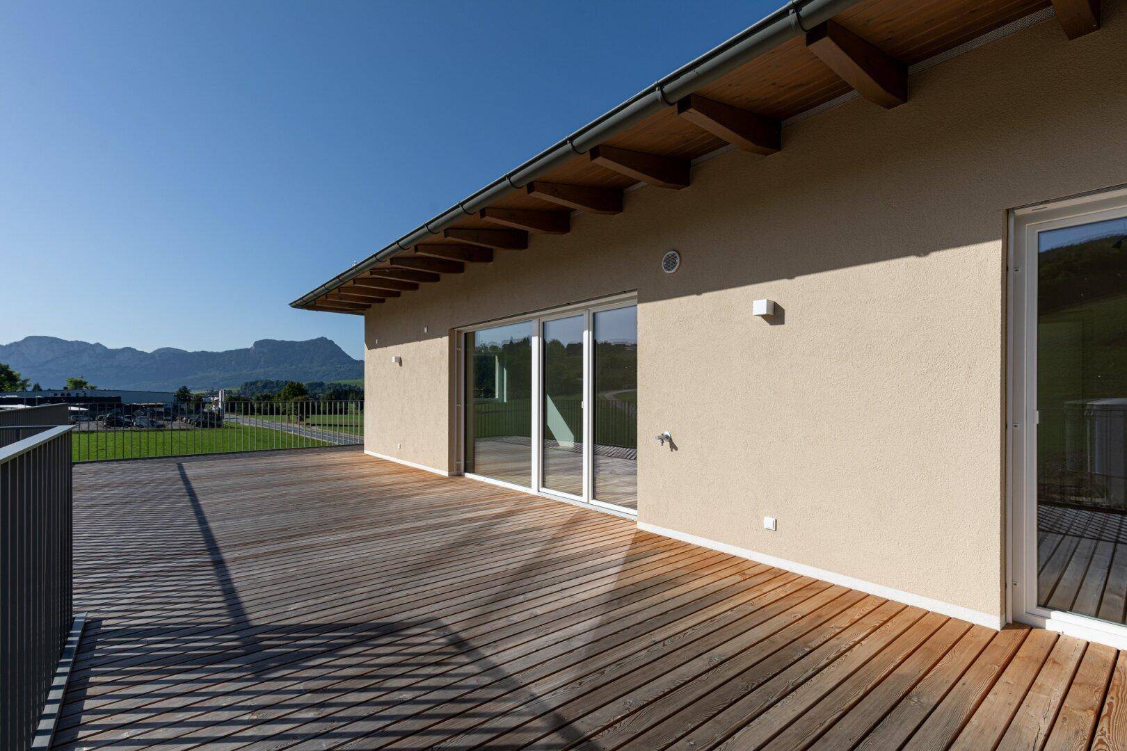 Große Holzterrasse mit Schiebetüren und Panoramablick auf die umliegende Berglandschaft.