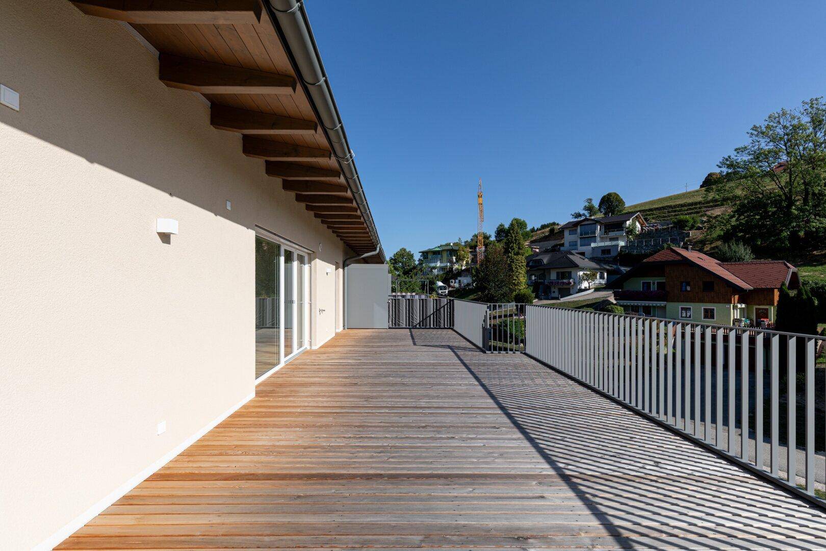 Weitläufige Holzterrasse mit moderner Brüstung und Blick auf die Nachbarschaft am Hang.