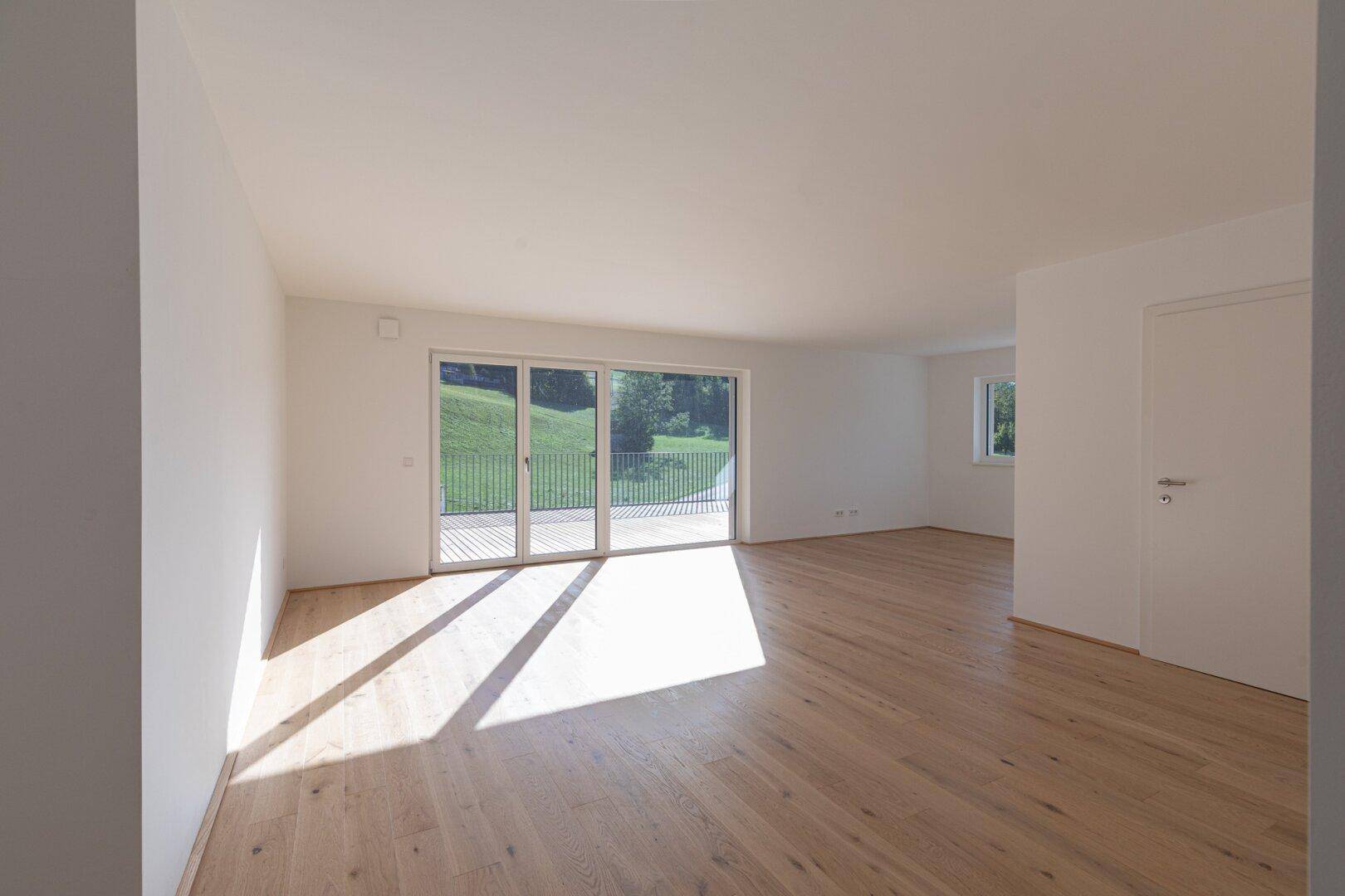 Lichtdurchfluteter Wohnraum mit hellem Holzboden und Zugang zu einem sonnigen Außenbereich.