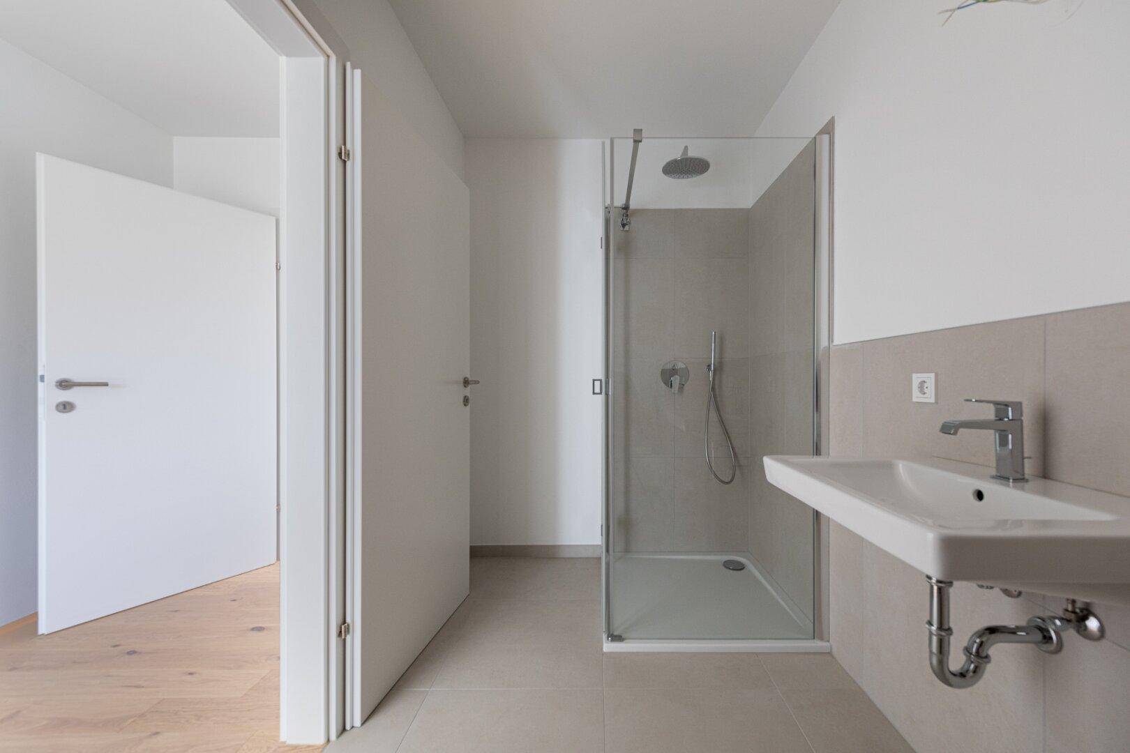 Modernes Badezimmer mit begehbarer Dusche, Einzelwaschbecken und hellen Fliesen.