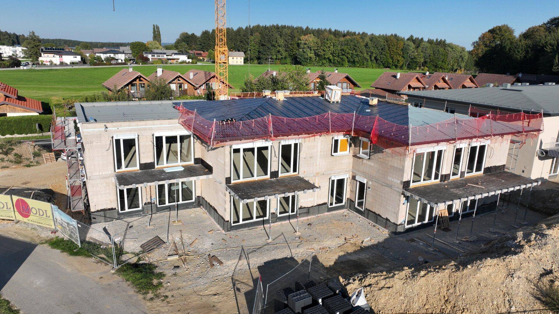 Nahaufnahme eines im Bau befindlichen Neubaus mit großen Fenstern und installierten Solarmodulen auf dem Flachdach.