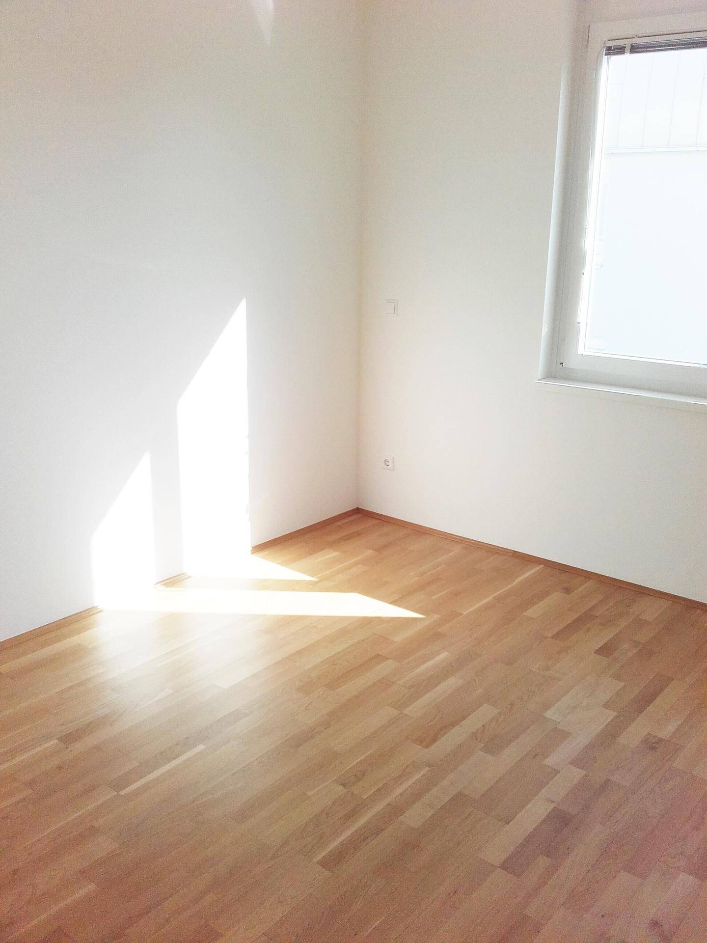 Sonnenverwöhntes Zimmer mit Parkettboden und großem Fenster, ideal als Schlafzimmer.