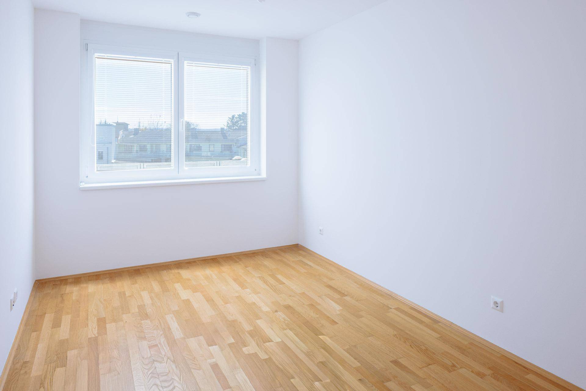 Helles Schlafzimmer mit zwei Fenstern, Parkettboden und weißen Wänden, bereit zum Einzug.