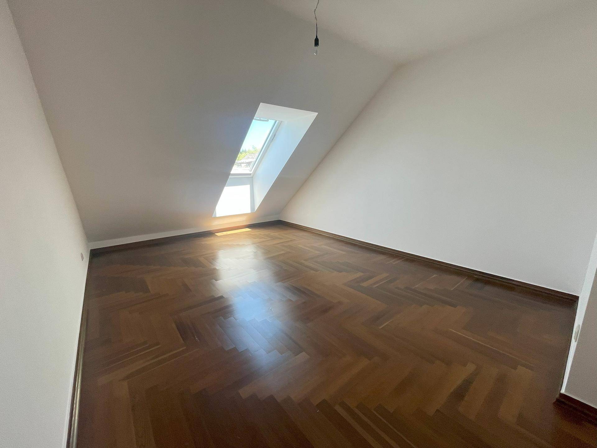 Helles Schlafzimmer im Dachgeschoss mit Dachfenster und Fischgrätparkett.