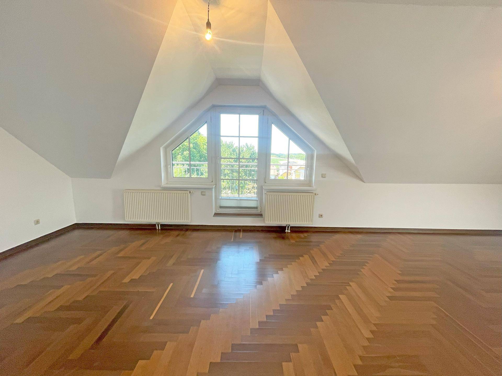 Helles Wohnzimmer im Dachgeschoss mit Fischgrätparkett und großen Fenstern.