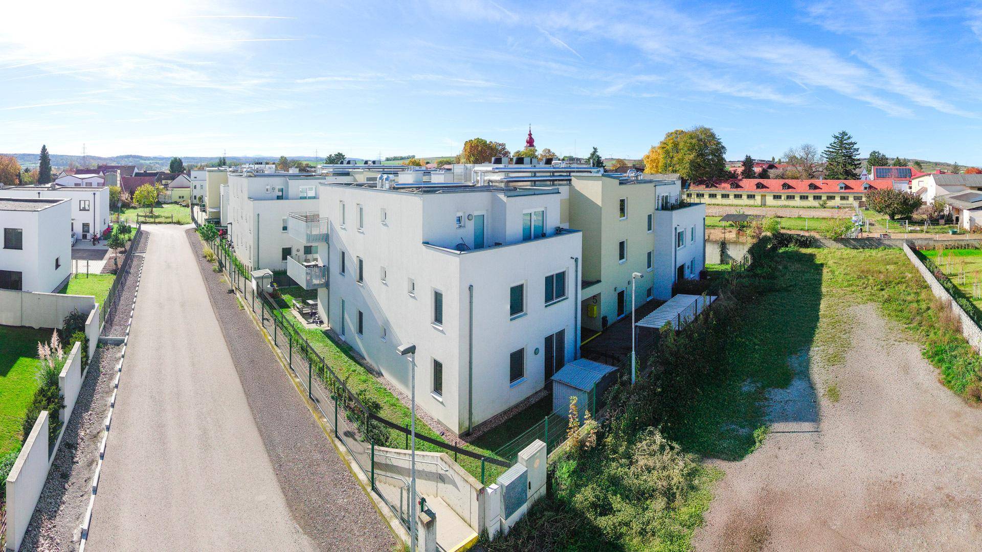 Luftaufnahme einer modernen Wohnsiedlung mit mehreren Gebäuden und viel Grün in ländlicher Umgebung.
