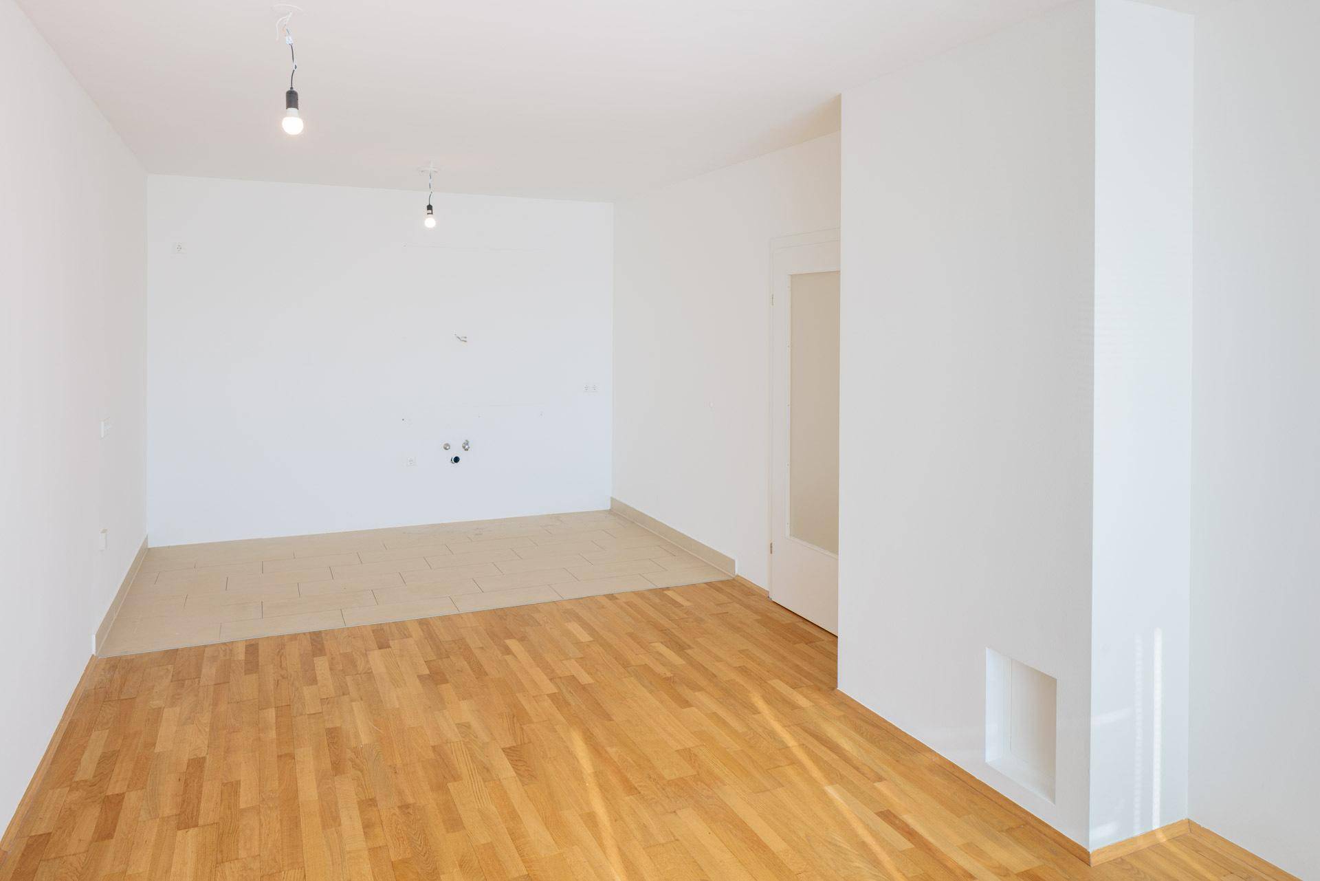 Geräumiger Raum mit Parkett- und Fliesenboden, vorbereitet für eine moderne Kücheninstallation.