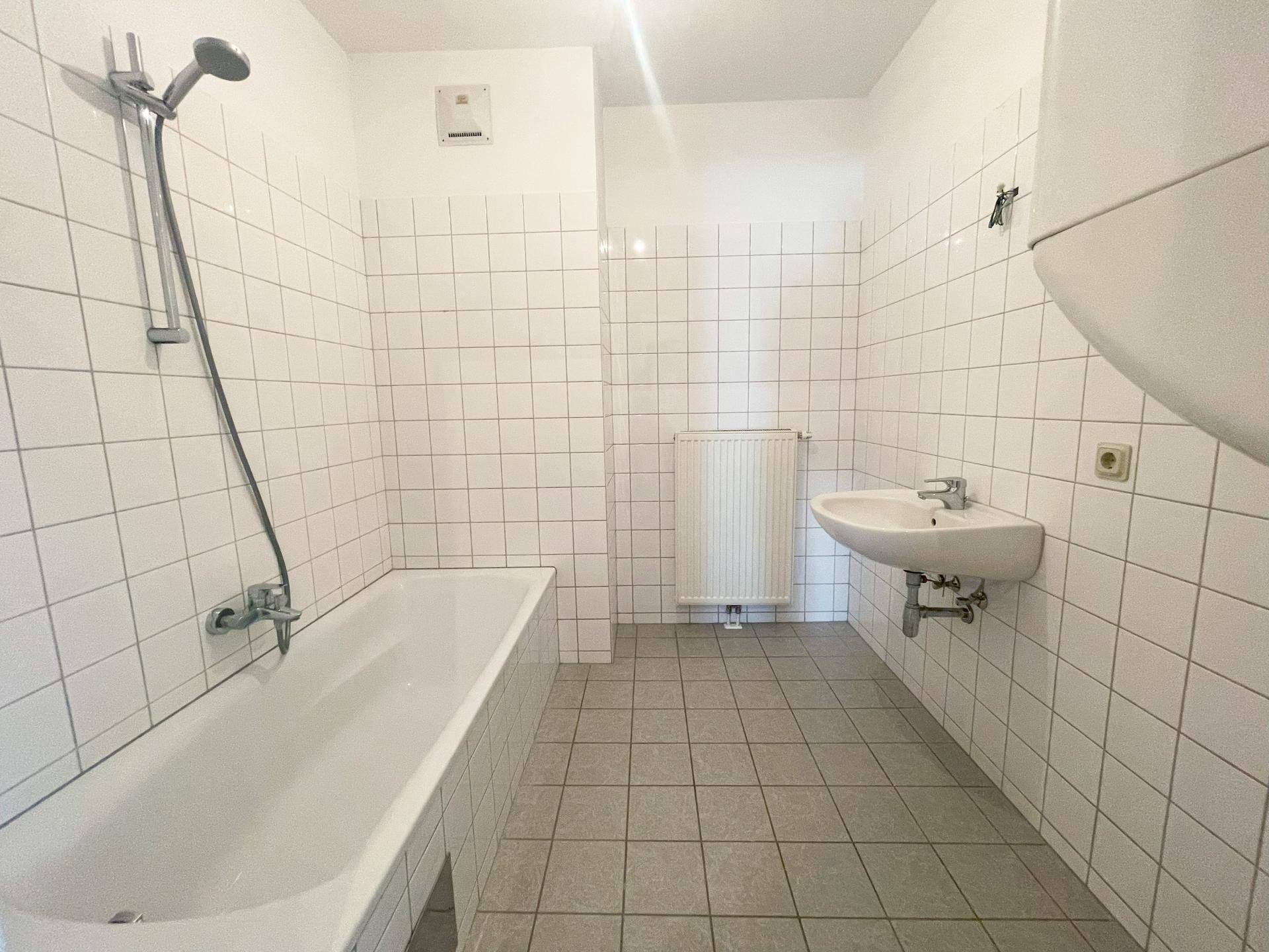 Funktionales Badezimmer mit Badewanne, Waschbecken und weißen Fliesen.