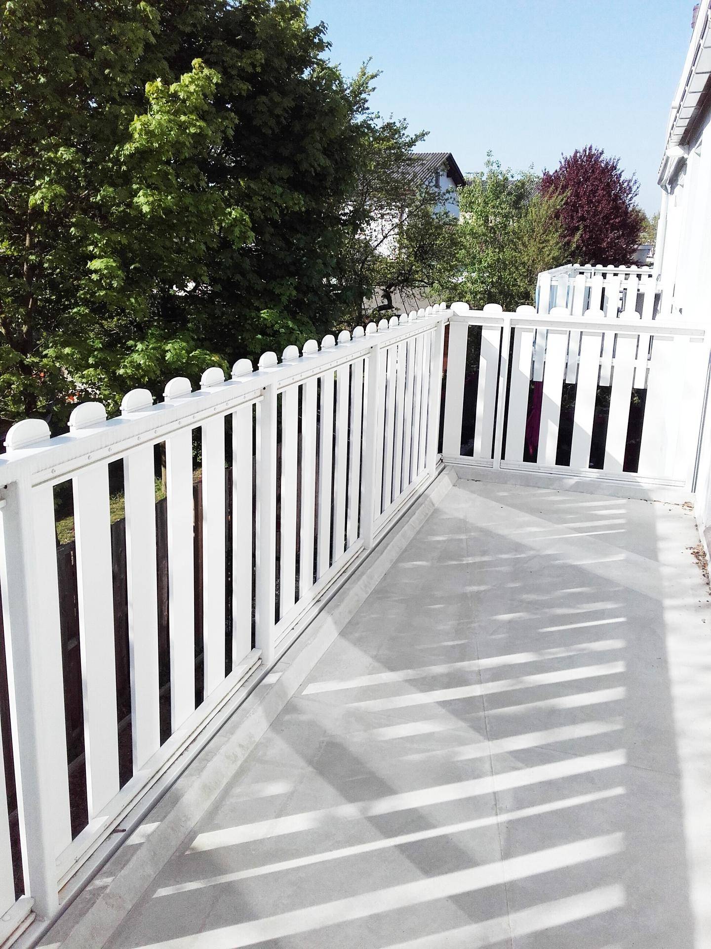 Geräumiger Balkon mit weißem Geländer und freiem Blick ins Grüne.