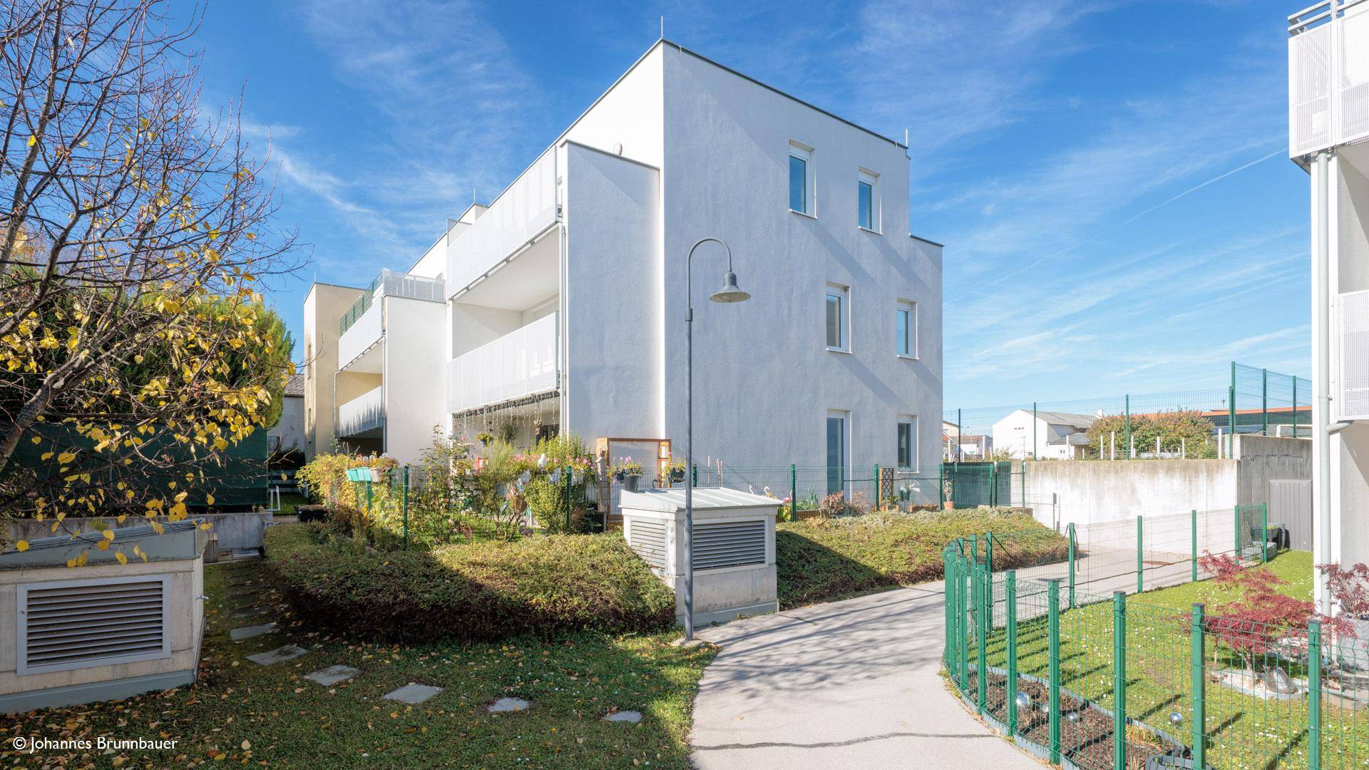 Moderne Wohnanlage mit weißer Fassade, umgeben von gepflegten Grünflächen und Wegen.