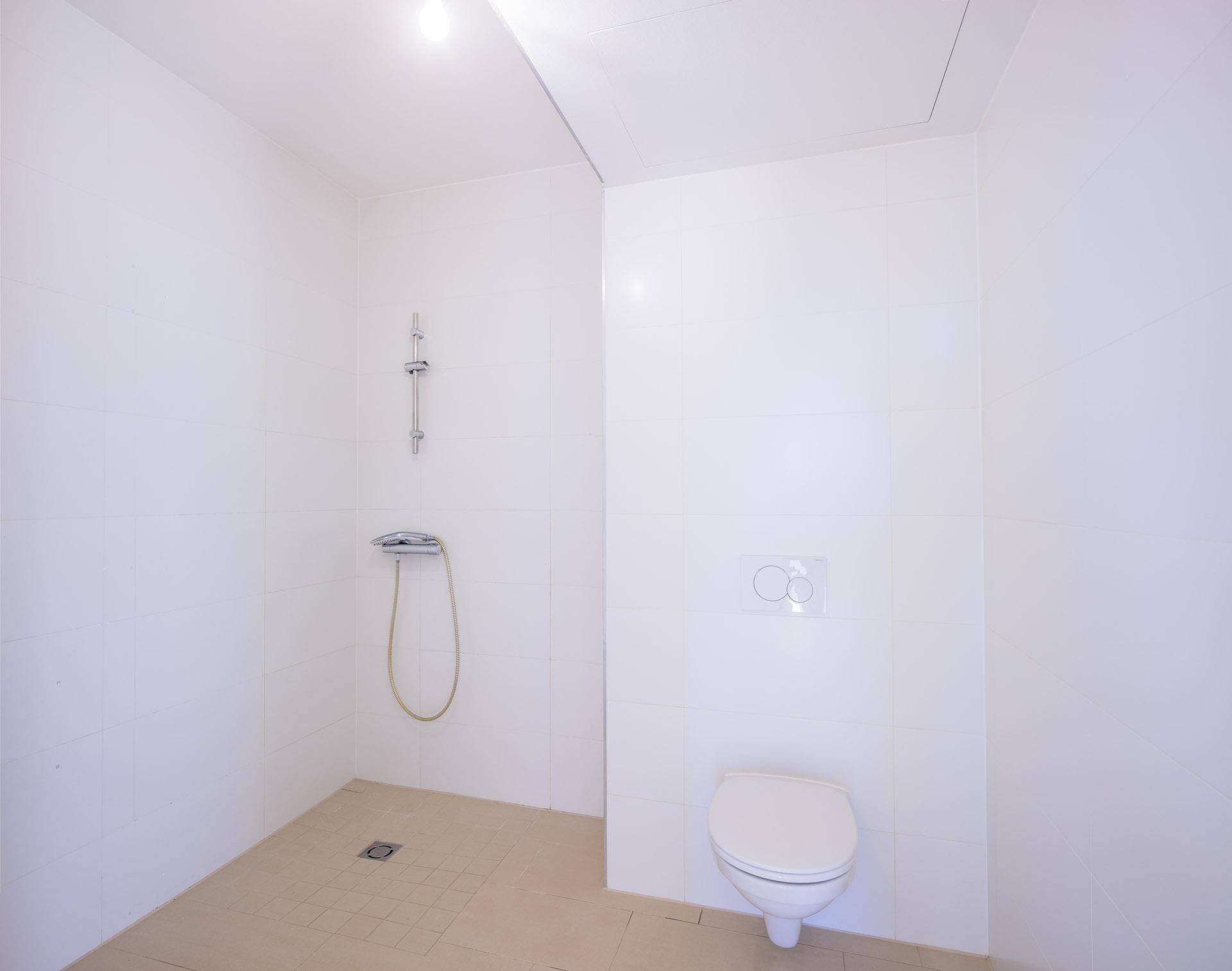 Helles Badezimmer mit Dusche und wandhängendem WC, komplett gefliest und funktional gestaltet.