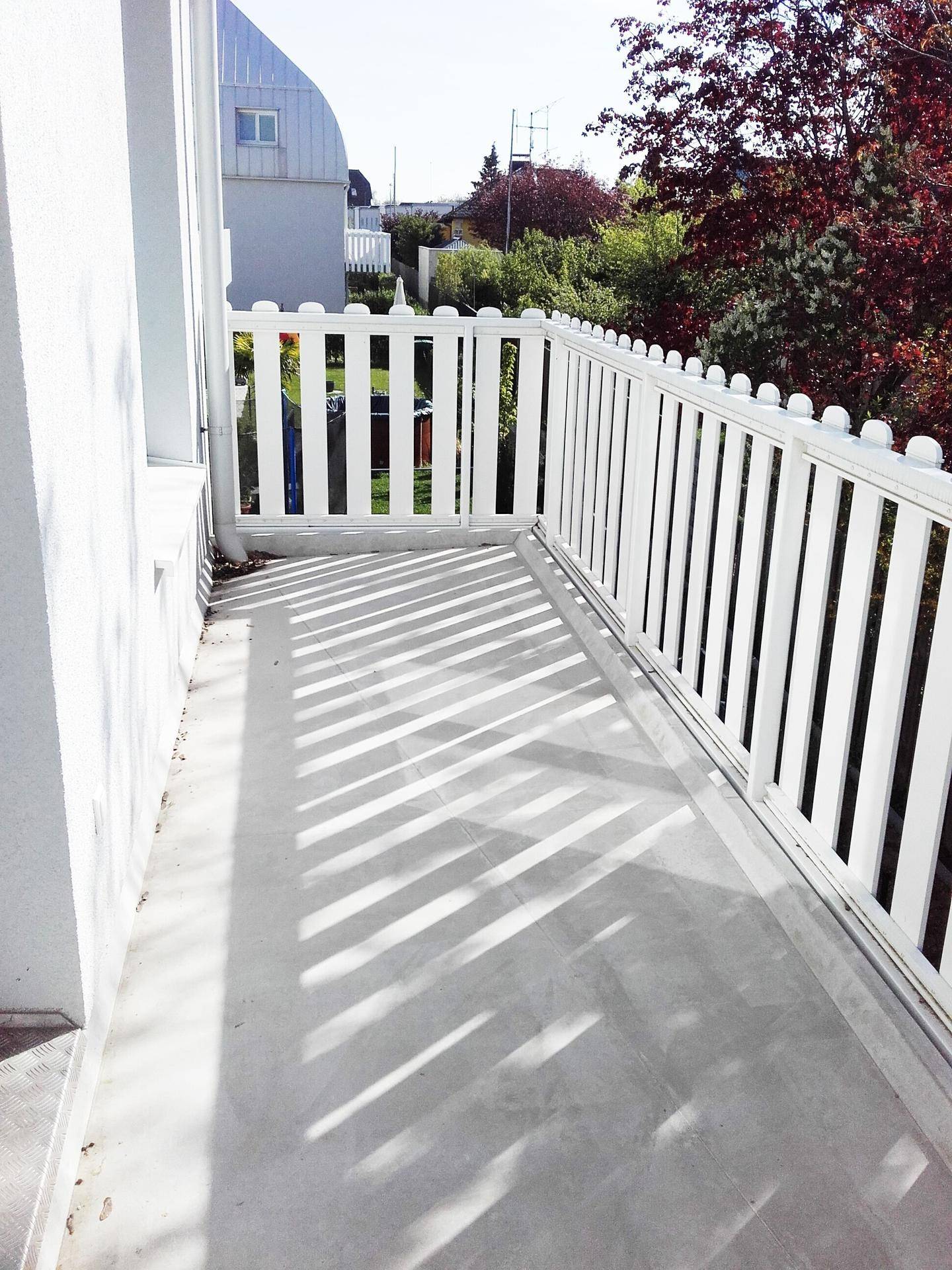 Langer Balkon mit weißem Geländer und viel Sonnenlicht, ideal zum Entspannen.