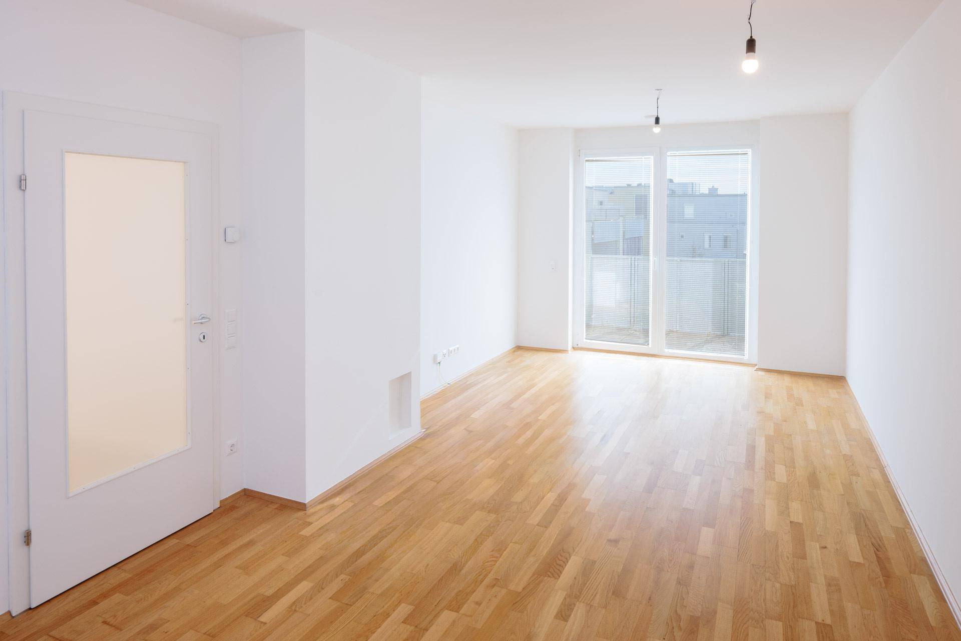 Helles Wohnzimmer mit Parkettboden und Zugang zu einem Balkon, bereit zur individuellen Gestaltung.