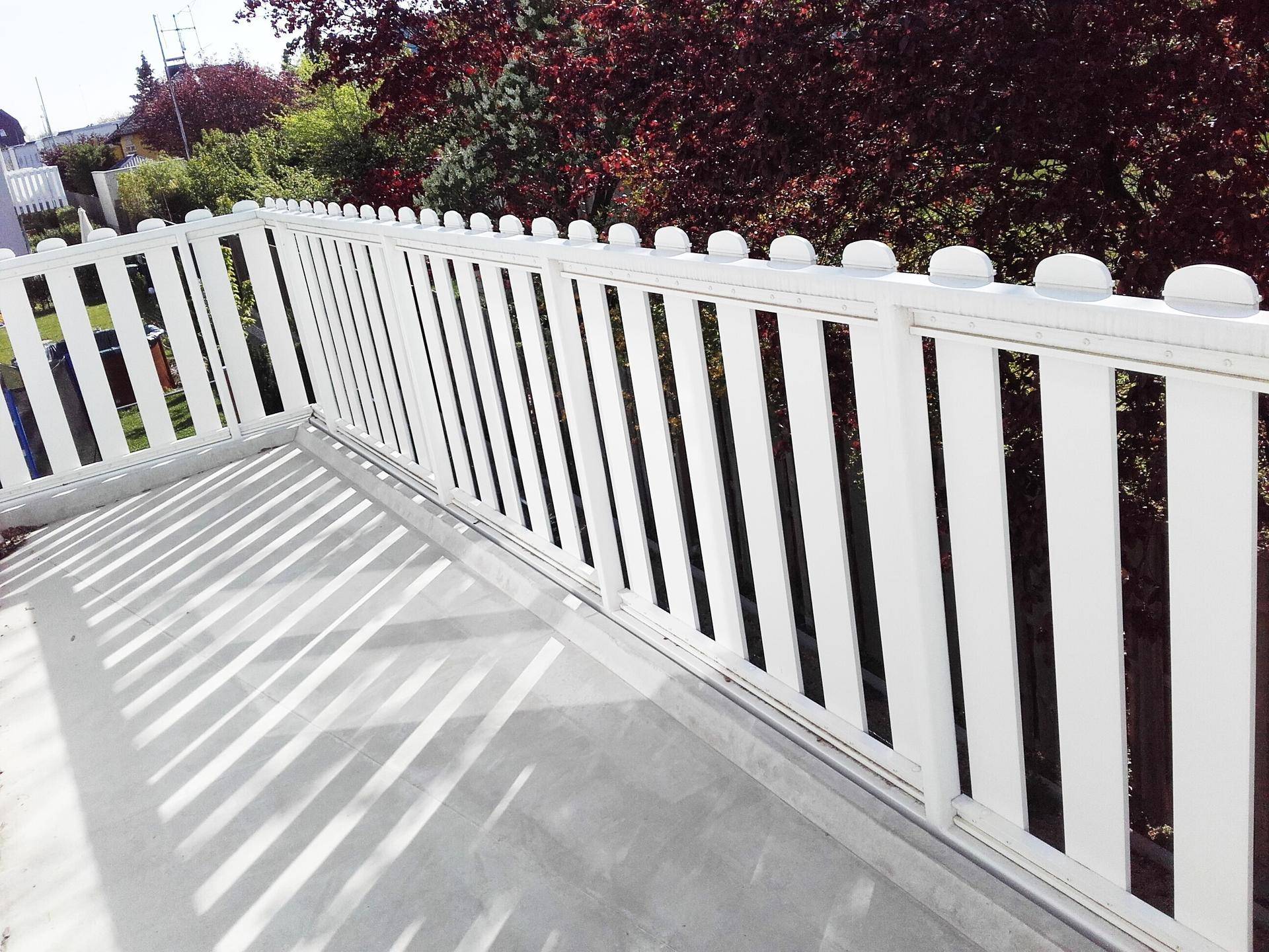 Sonniger Balkon mit weißem Geländer und Blick auf die umliegende Vegetation.