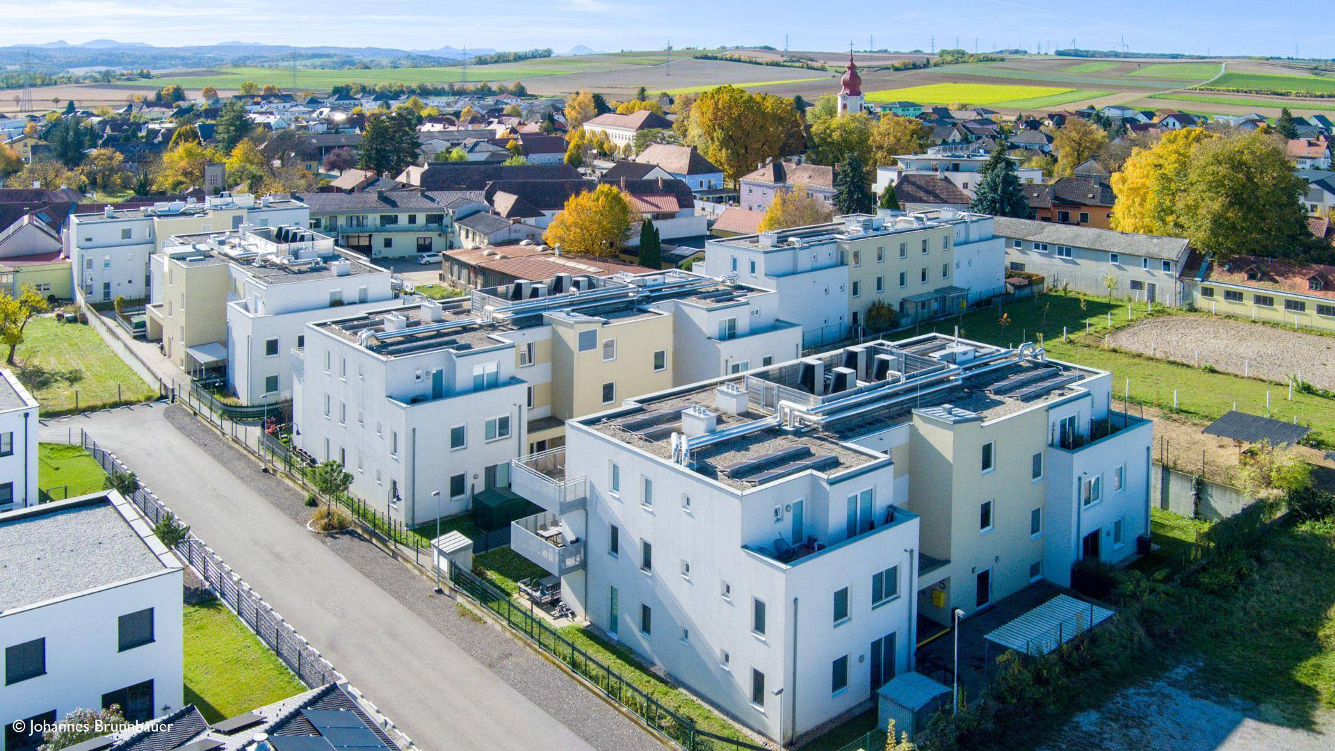 Luftaufnahme einer modernen Wohnsiedlung mit mehreren Gebäuden und ländlicher Umgebung.