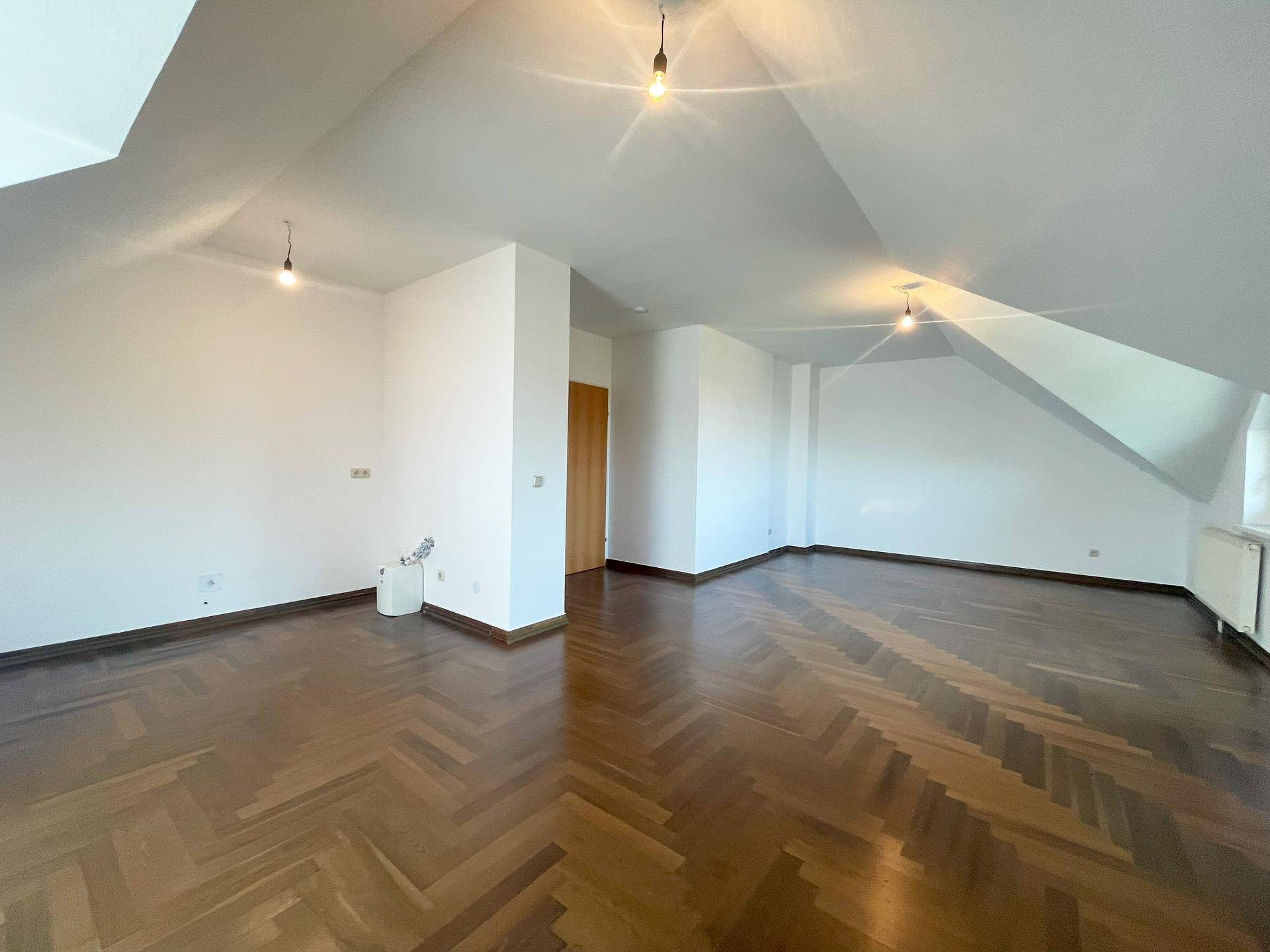 Heller Dachgeschossraum mit Holzboden und Zugang zu weiteren Bereichen des Apartments.