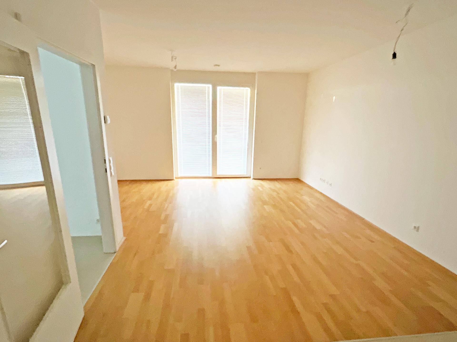 Geräumiges, helles Wohnzimmer mit Parkettboden und Zugang zu einem Außenbereich.