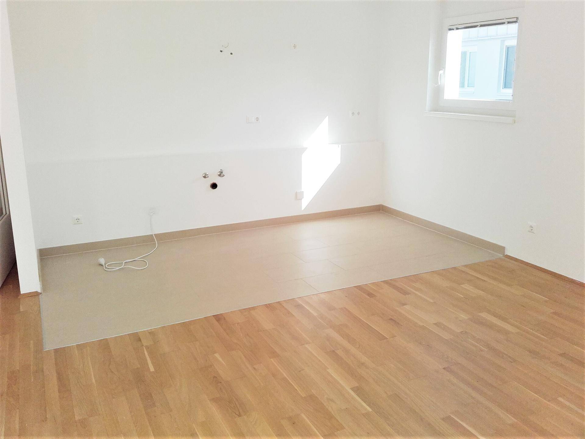 Helle Küche mit Parkett- und Fliesenboden, vorbereitet für die Installation einer Einbauküche.