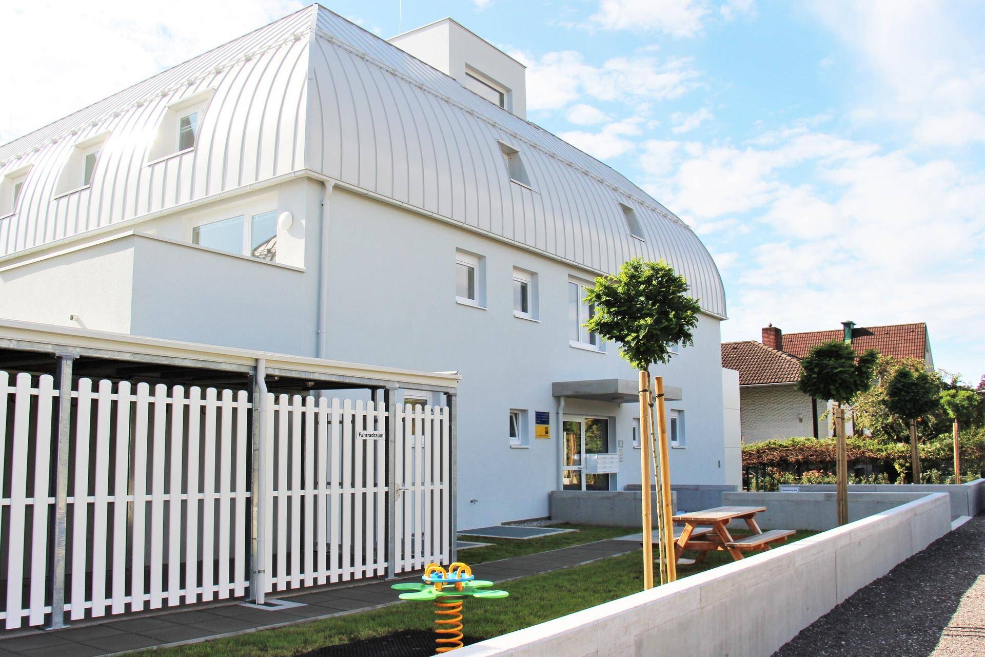 Modernes Gebäude mit markantem Runddach und Spielbereich im Außenbereich.