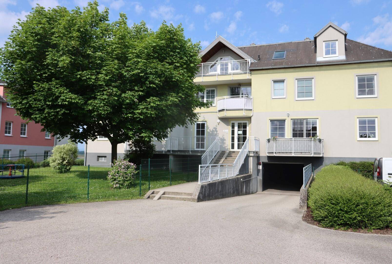Mehrfamilienhaus mit Balkonen, Grünflächen und Zufahrt zur Tiefgarage.