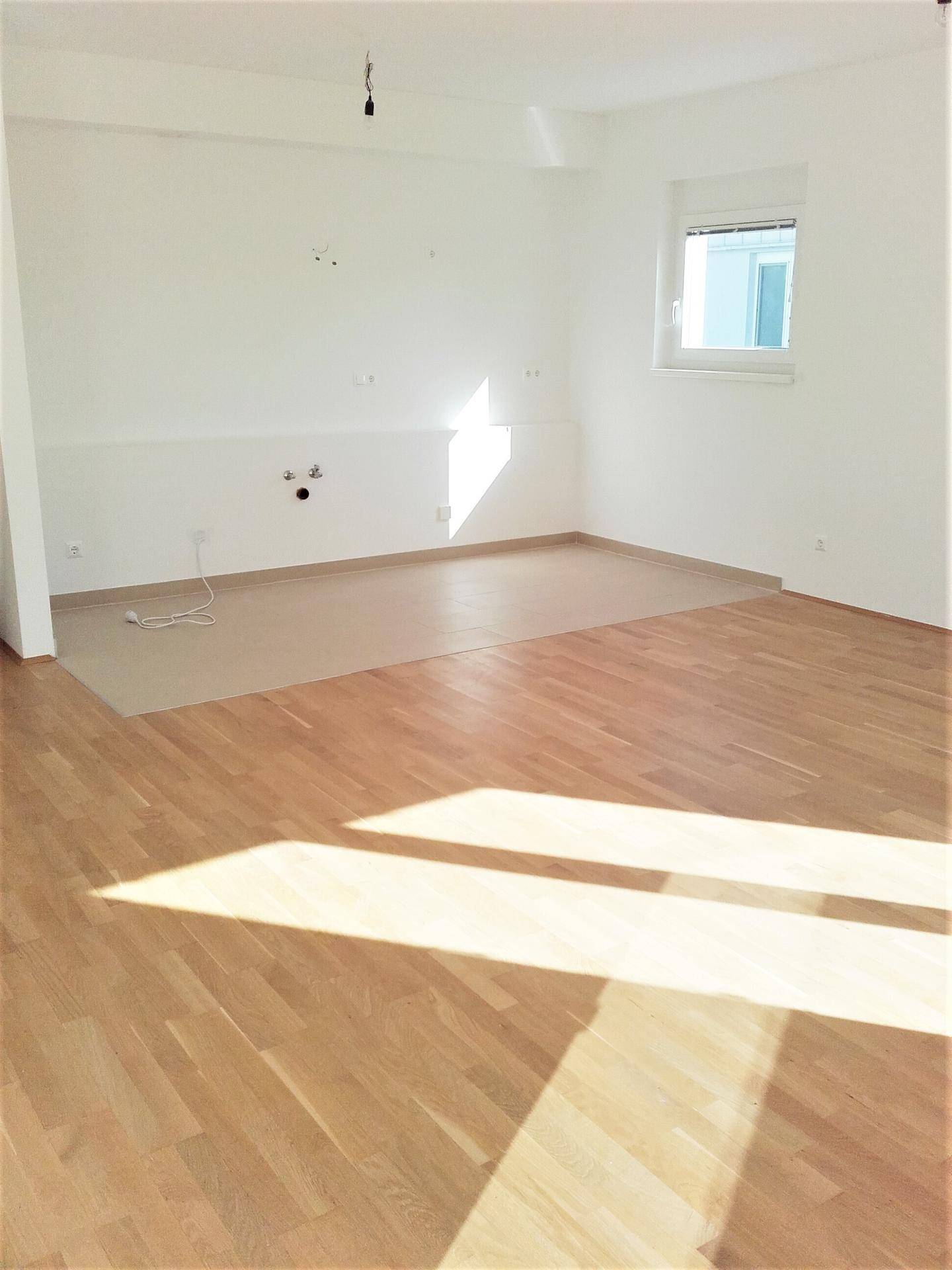 Sonnenbeschienene Küche mit kombiniertem Parkett- und Fliesenboden und Fenster.