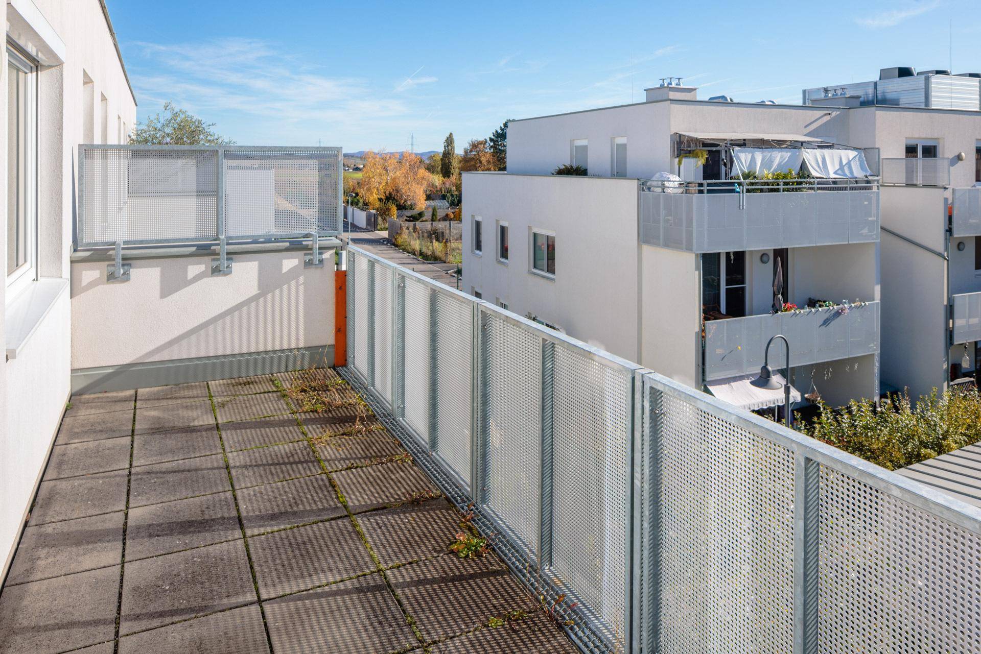 Heller Balkon mit Metallgeländer und Ausblick auf benachbarte moderne Wohngebäude.