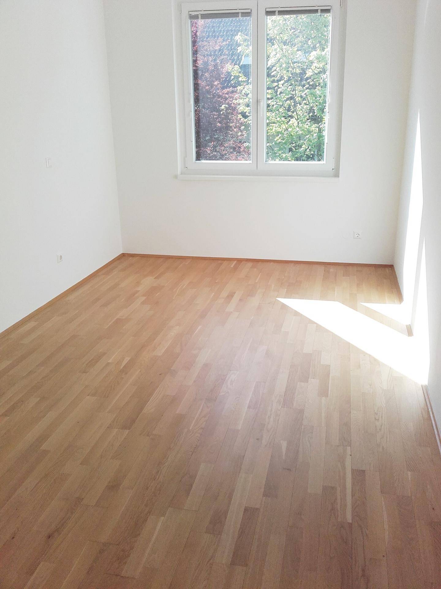 Helles Schlafzimmer mit Parkettboden und Fenster mit Blick ins Grüne.