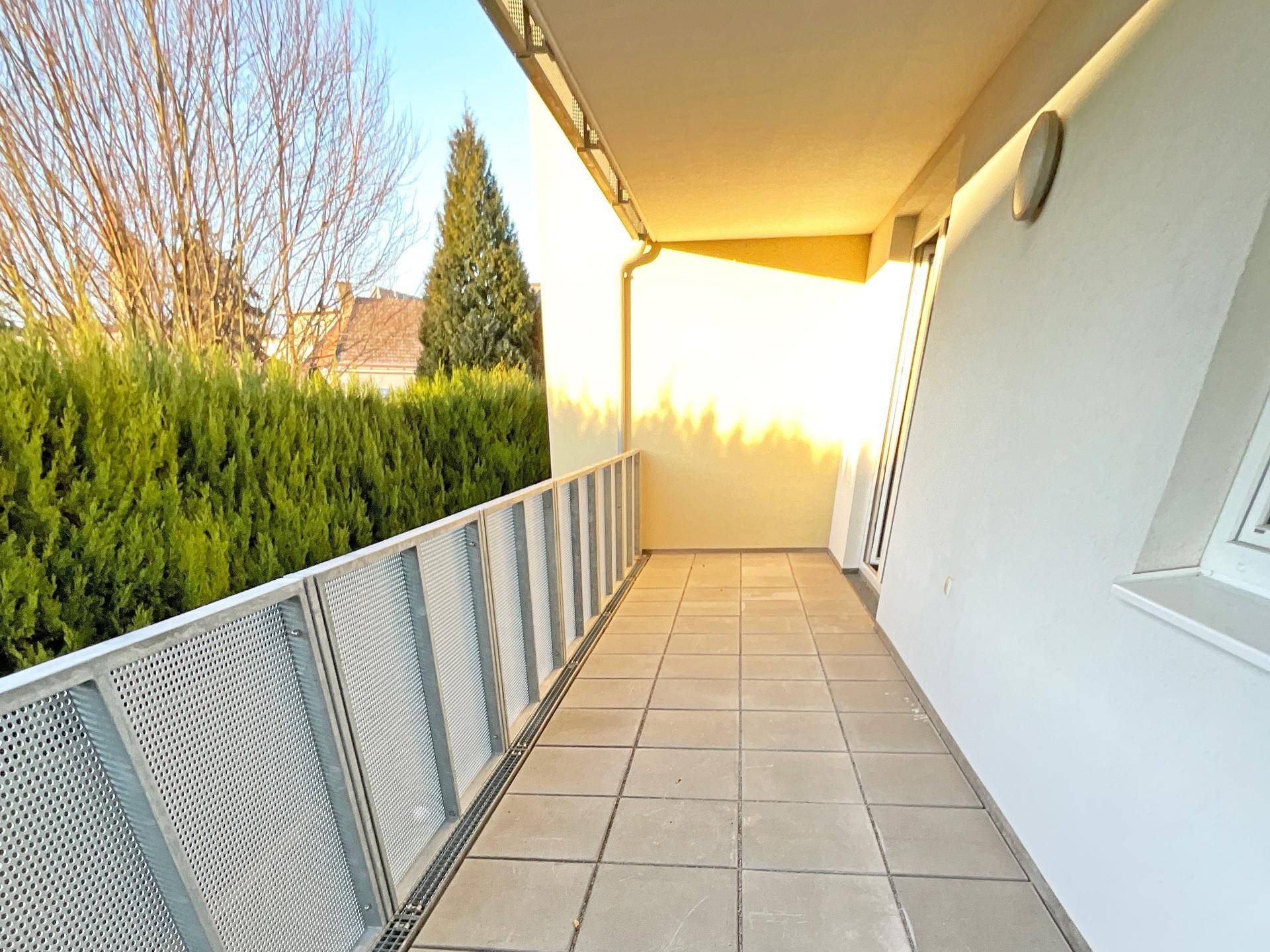 Heller Balkon mit Fliesenboden und Blick ins Grüne, umgeben von einer gepflegten Hecke.