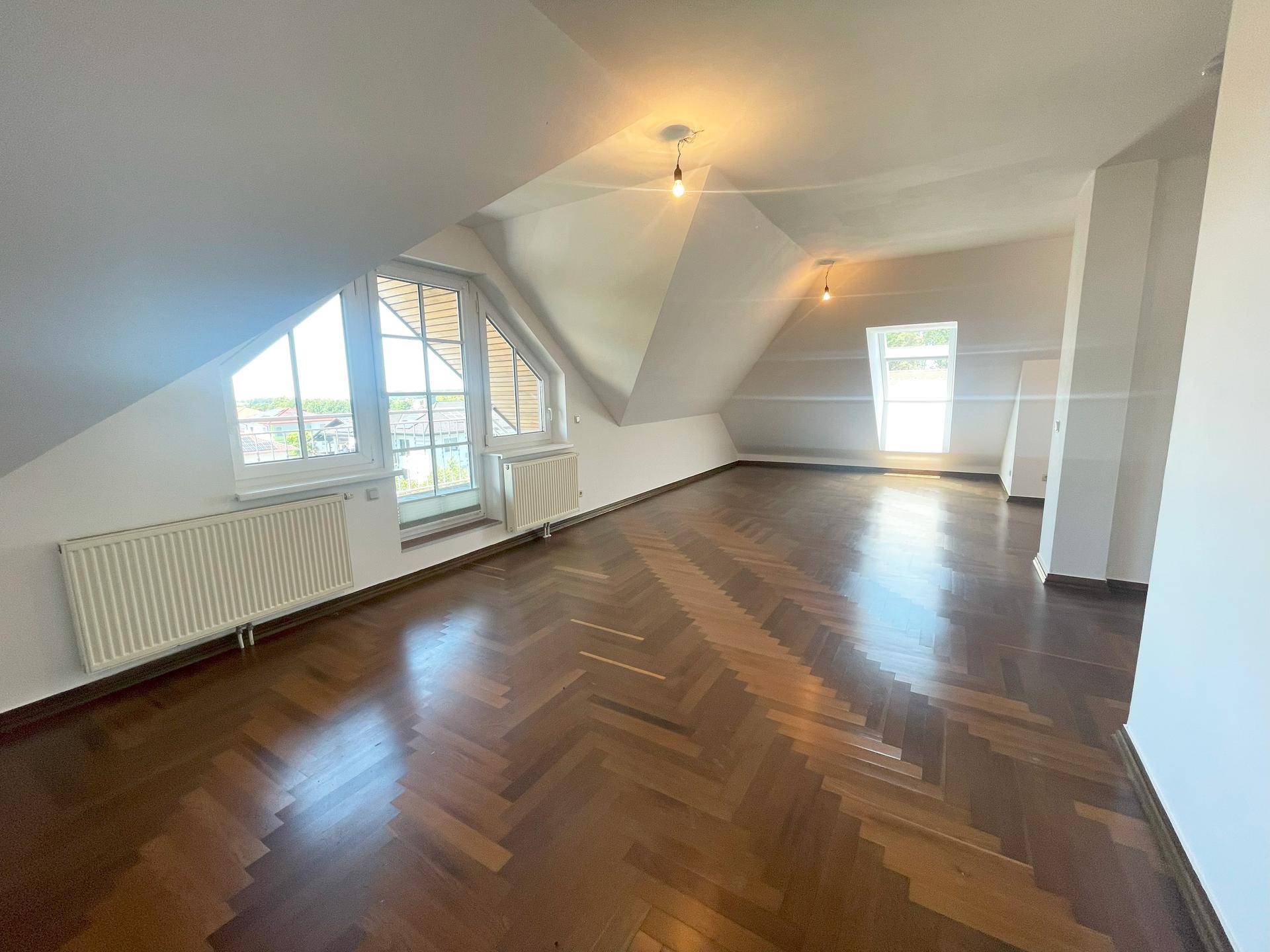Geräumiges Dachgeschosszimmer mit schrägen Wänden, Parkettboden und viel Tageslicht.