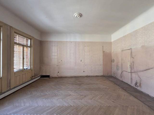 Großes Zimmer mit Fischgrätparkett und einem Fenster mit Jalousien, das renoviert werden muss.