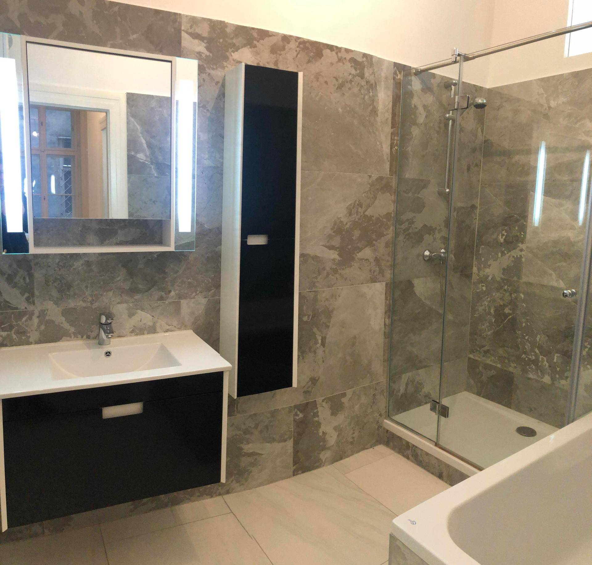 Modernes Badezimmer mit grauen Marmorfliesen, Waschtisch, Spiegelschrank, Duschkabine und Badewanne.
