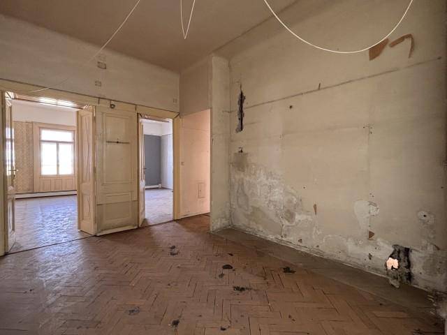 Renovierungsbedürftiges Zimmer mit Fischgrätparkett und beschädigten Wänden, das Potenzial bietet.