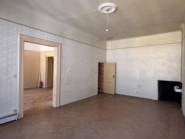 Unrenoviertes Wohnzimmer mit Fischgrätparkett, Stuckdecke und Tapetenresten, bereit zur Sanierung.