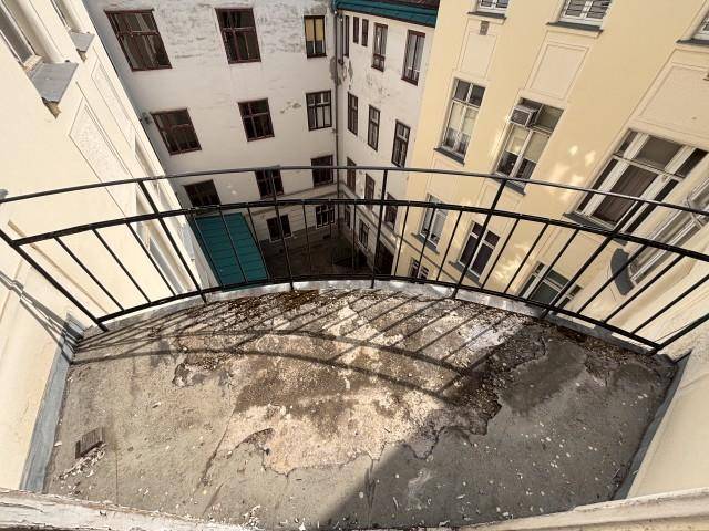Kleiner Balkon mit Blick auf den Innenhof eines Altbaus, der eine Renovierung benötigt.