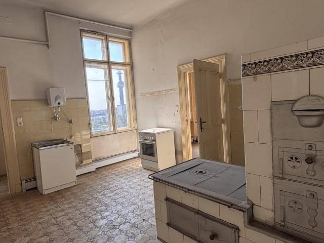 Alte Küche mit Kachelofen, Fliesenboden und Blick auf die Stadt durch das Fenster, bereit zur Renovierung.