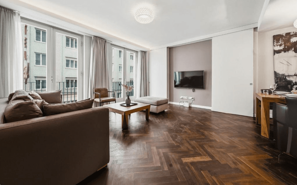 Helles Wohnzimmer mit Fischgrätparkett, TV und Zugang zum französischen Balkon.