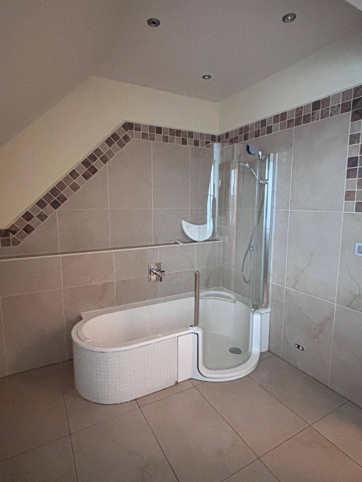 Modernes Badezimmer mit Duschkabine, Badewanne und beigefarbenen Fliesen an Wänden und Boden.