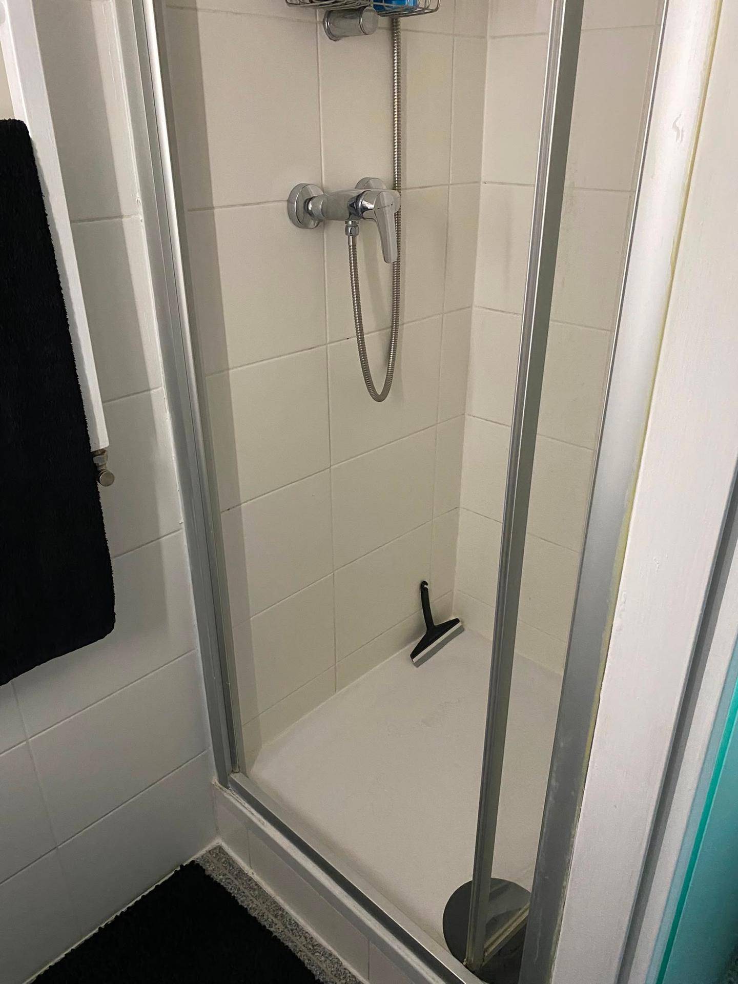 Duschkabine mit weißen Fliesen und einer einfachen Duscharmatur in einem kompakten Badezimmer.