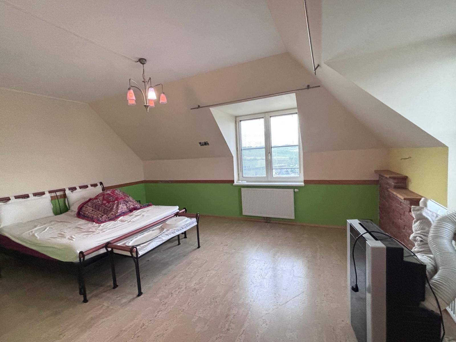 Schlafzimmer im Dachgeschoss mit Bett, grünen Wänden, Holzboden und einem Fenster mit Ausblick.