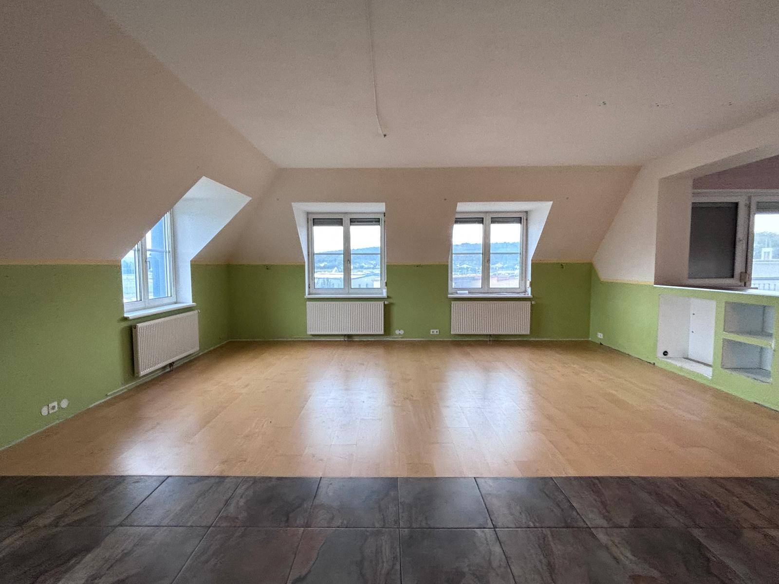 Großer, heller Raum im Dachgeschoss mit Holzboden und Fliesen, grünen Wänden und Dachschrägen.