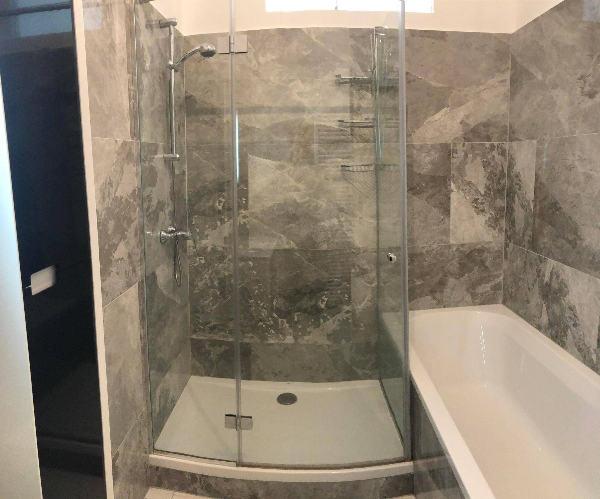Geräumige Duschkabine und Badewanne in einem elegant gefliesten Badezimmer mit modernen Armaturen.