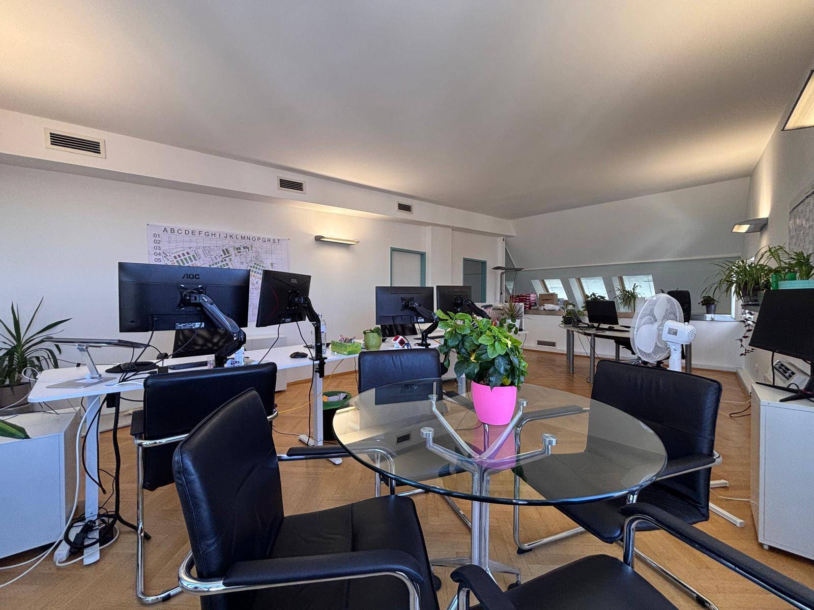 Heller Büroraum mit Glas-Besprechungstisch, mehreren Computerarbeitsplätzen und Dachfenstern.
