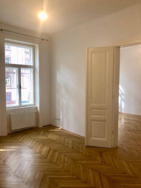 Helles Zimmer mit großem Fenster, Heizkörper und klassischem Fischgrätparkett, ideal als Wohnraum.